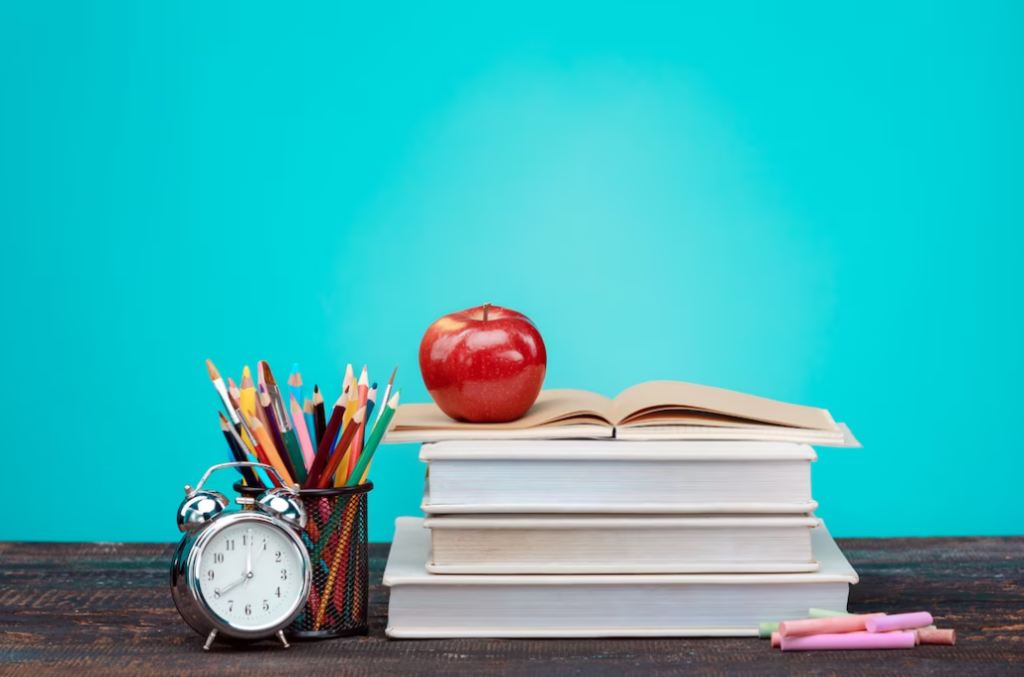 stock of books with apple on them, the clock, and colorful pencils near the book 